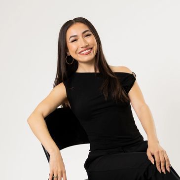 Woman in black dress sitting on a chair, smiling.