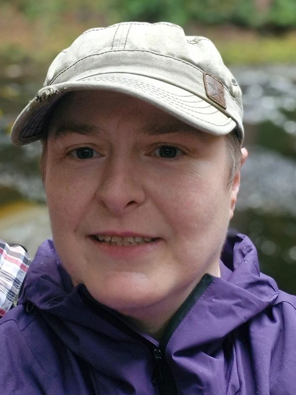 Person wearing a gray cap and purple jacket smiling outdoors.