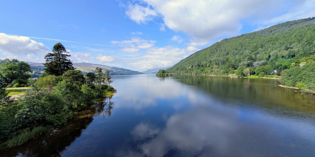 Calm river flanked by green forests under a partly cloudy sky.