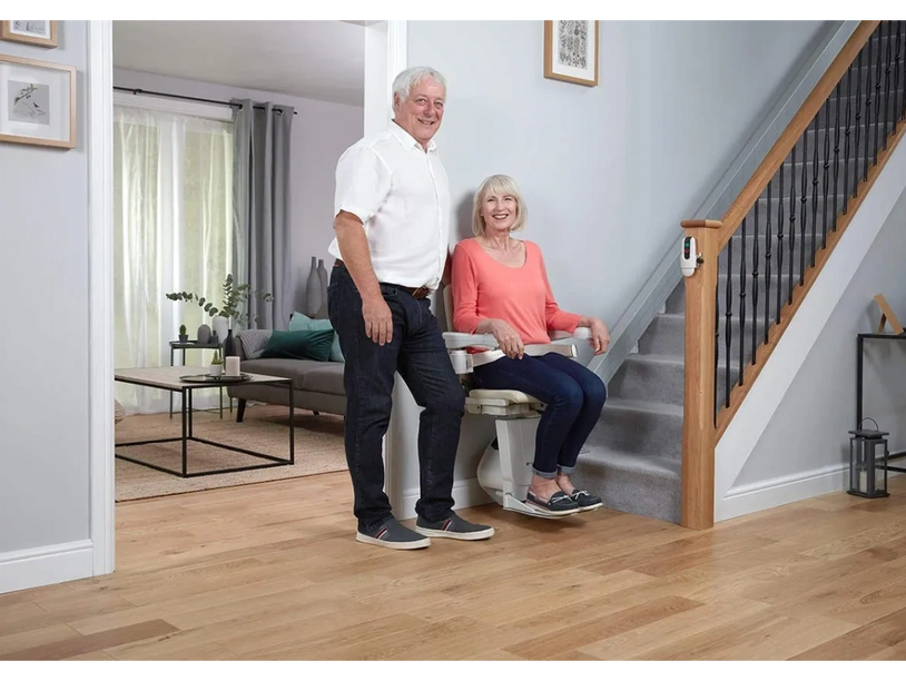 Couple at the foot of their stairs. Lady sat in a straight stairlift.