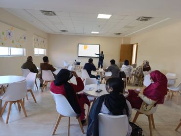 People attending a presentation in a modern, well-lit room with white chairs.