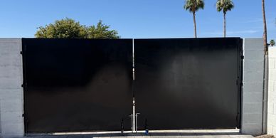 Large black metal gate between two concrete walls.