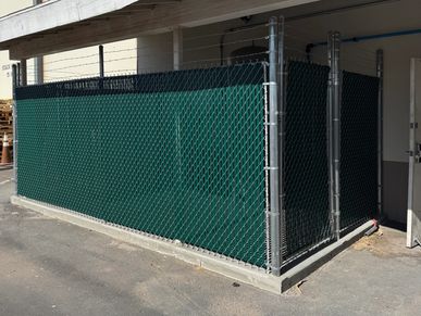 Chain-link fence with green privacy screen around a corner.