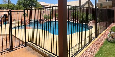 Backyard pool with black safety fence and palm trees.