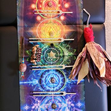 A colorful chakra-themed cloth with crystals and a smudge stick.