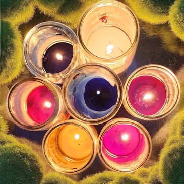 Seven colorful candles burning in glass jars arranged in a circle.