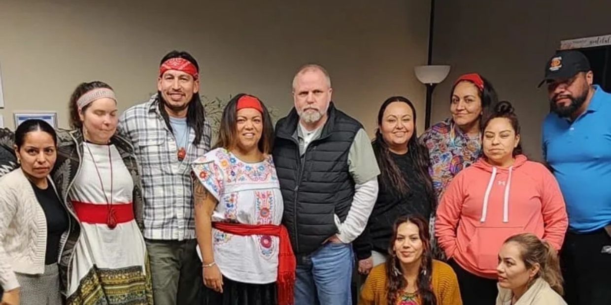 A diverse group of people posing together indoors, some wearing traditional clothing.