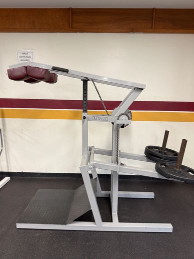 A seated calf raise machine in a gym with weights on the sides.