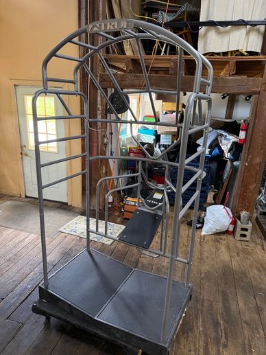 Metal frame structure resembling a chair or cage in a cluttered room.