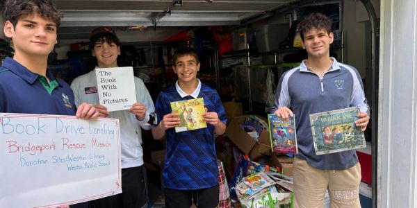 Four boys holding books and a donation sign for a book drive.