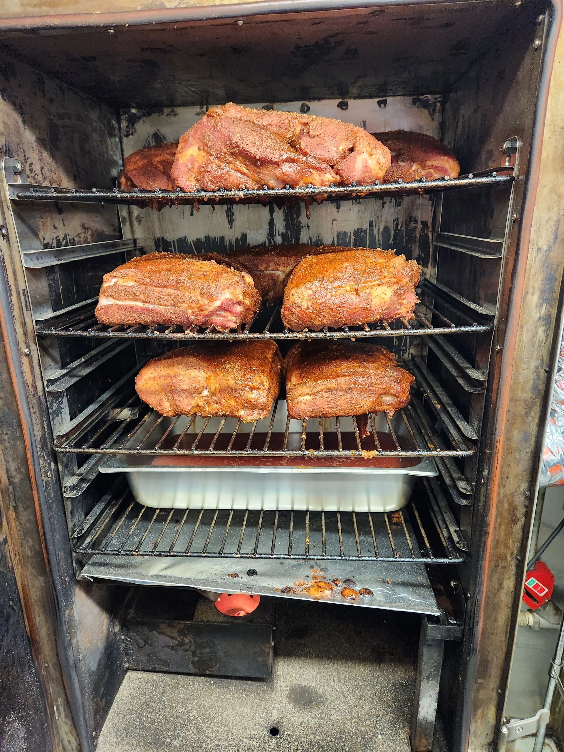 Multiple slabs of seasoned meat smoking inside a smoker.