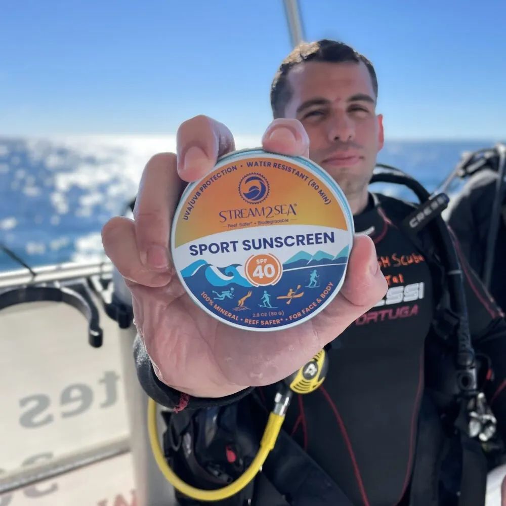 A diver on a boat holding up Stream2Sea sunscreen.