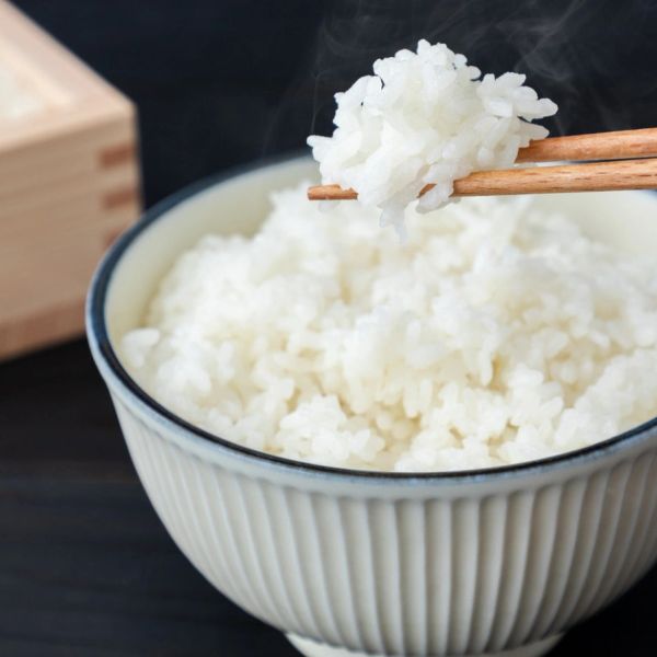 Steaming white rice held by chopsticks above a bowl.