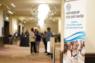 Banner for Partnership for Safe Water at a conference with attendees in background.