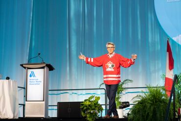 Speaker in red hockey jersey on stage at conference.