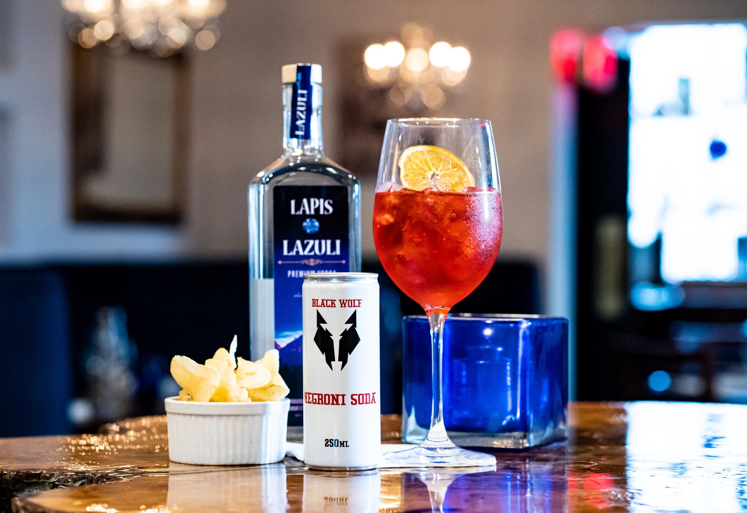 A refreshing Negroni cocktail with chips and soda on a wooden table.