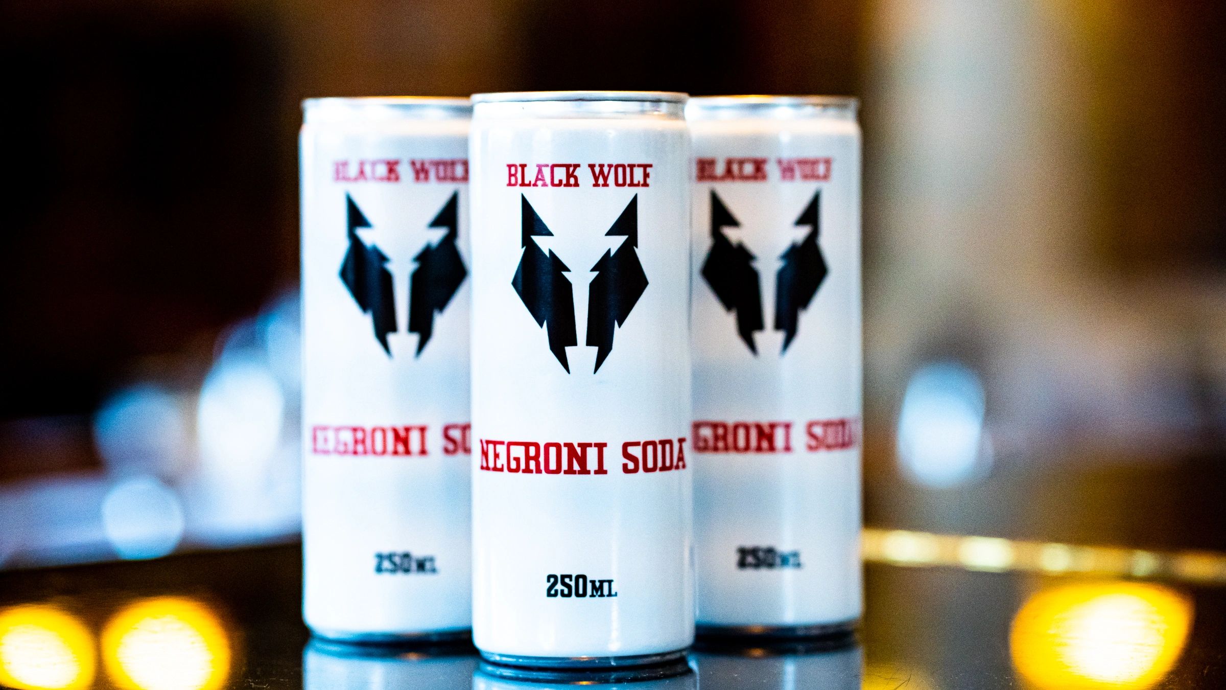 Three cans of Black Wolf Negroni Soda with a wolf logo.