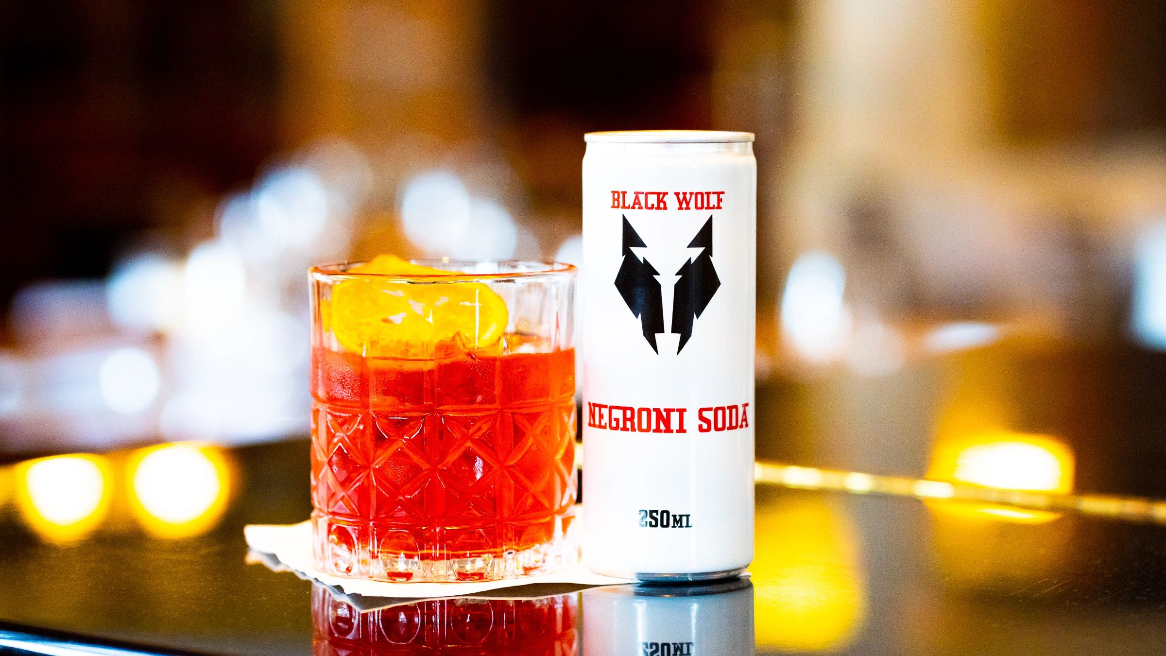 A can of Black Wolf Negroni Soda next to a glass with an orange garnish.