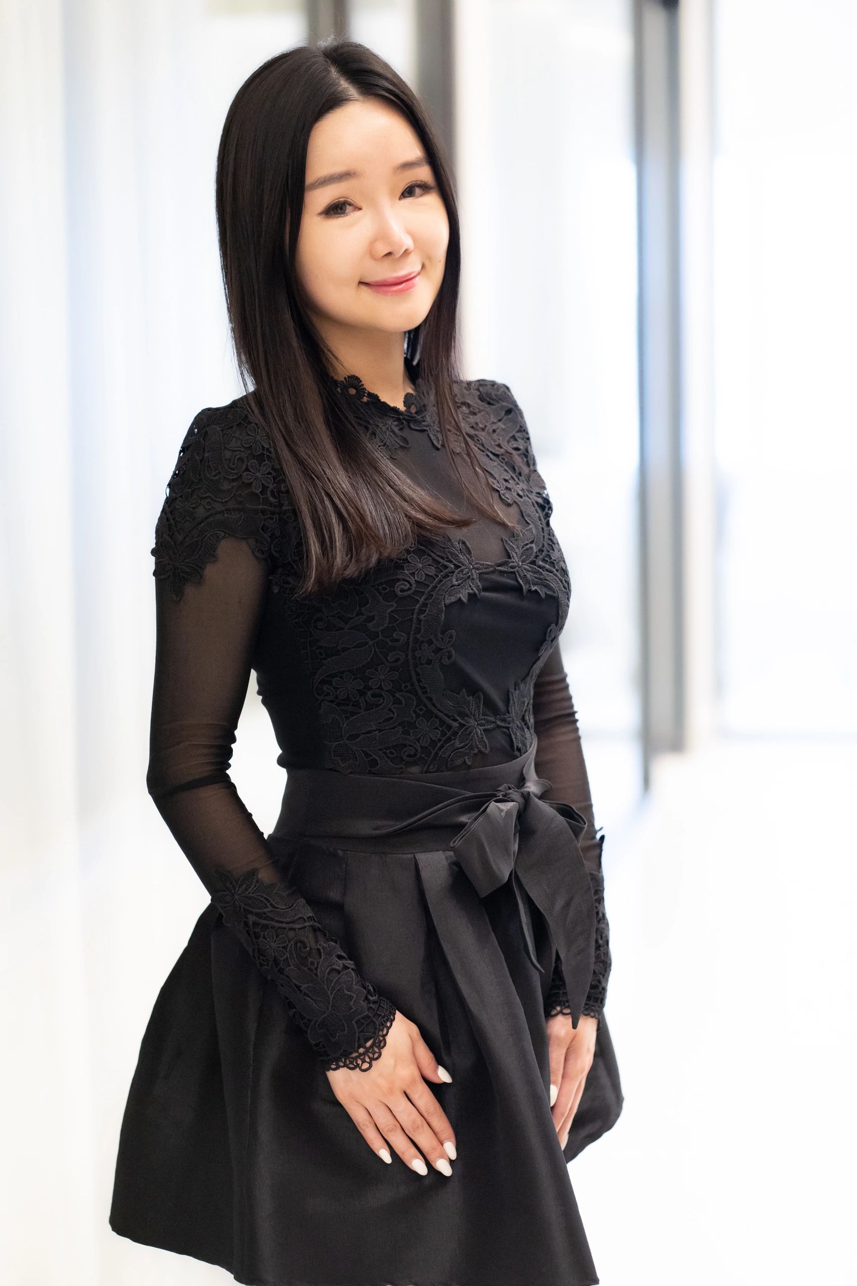 Smiling woman in elegant black lace dress with sheer sleeves.