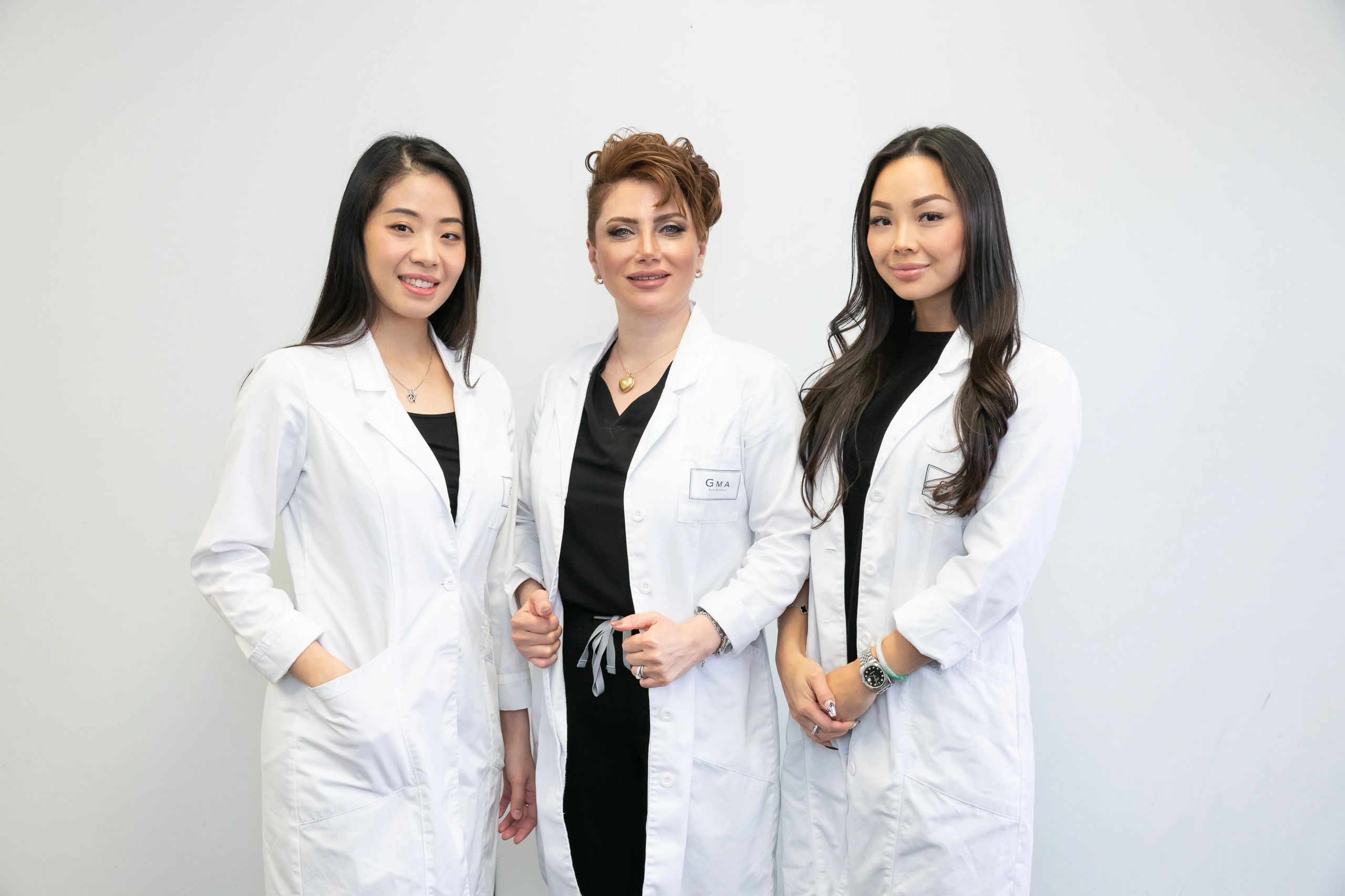 Three women in white medical coats posing confidently together.