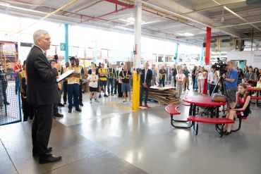 Man speaking to a crowd in a warehouse setting.