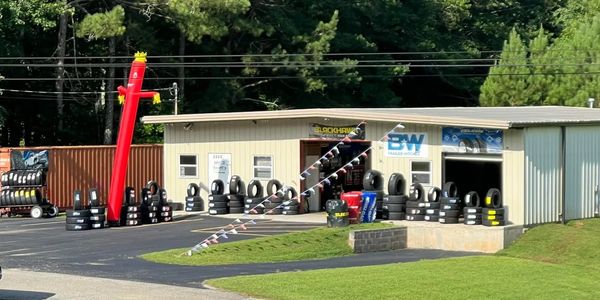 Tire shop with stacks of tires and inflatable tube man outside.