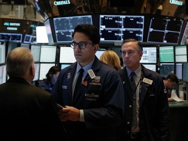 Traders working on the busy floor of a stock exchange with multiple monitors.