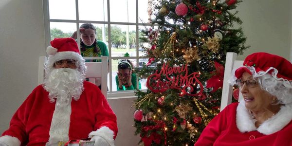 Santa and Mrs. Claus sit by a Christmas tree while kids peek through the window.