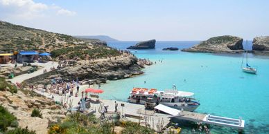 alt="Blue lagoons of Comino and Gozo, Malta with turquoise waters, boats, and swimmers enjoying"