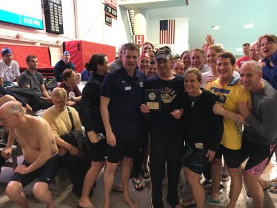 A group of swimmers celebrating a victory with a trophy at a pool.