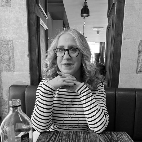 Woman with glasses and curly hair sitting at a wooden table in a cafe.