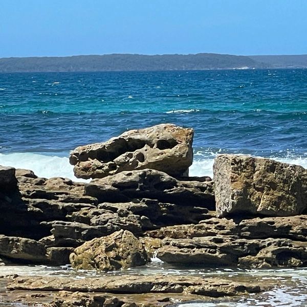 Rocky shore with waves and clear blue ocean under a bright sky.