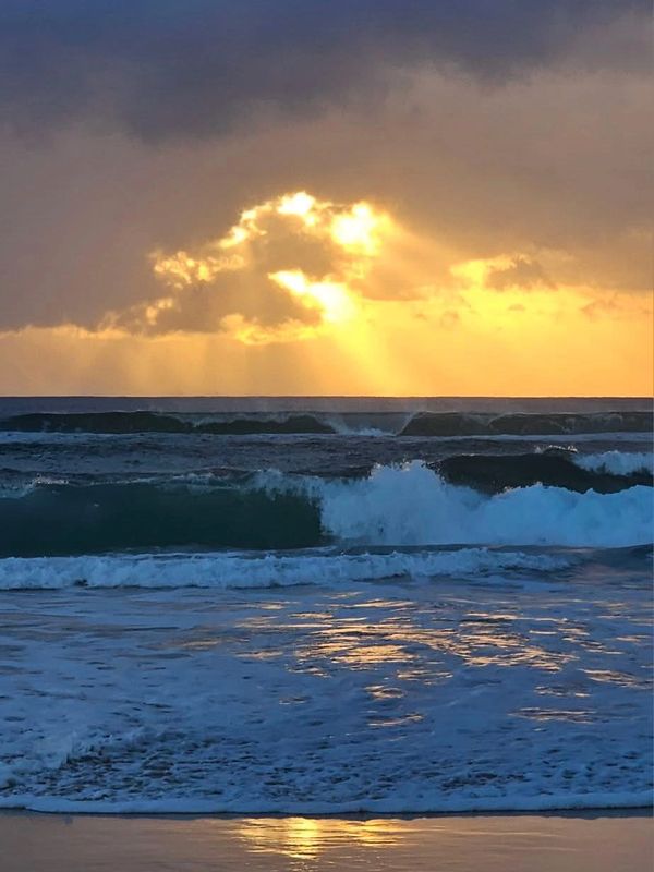 Sunset over crashing ocean waves with golden light.