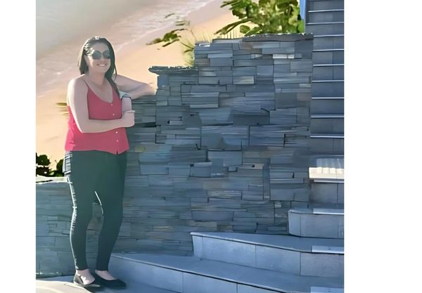 Woman in red top and sunglasses beside stone stairs and wall.