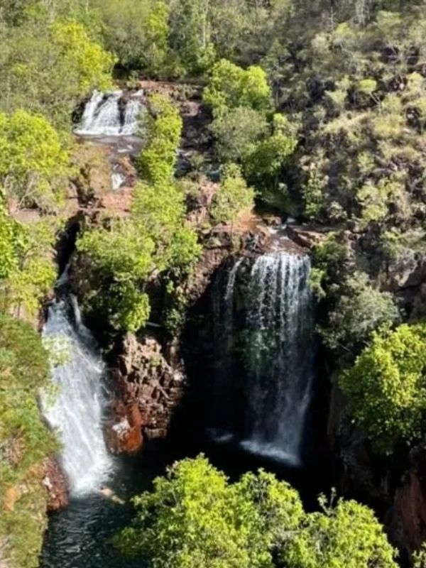 Two waterfalls cascading through lush green foliage in a rocky landscape.