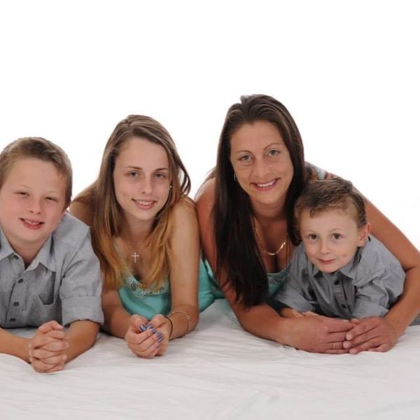 A smiling woman with three children lying on a white surface against a white background.