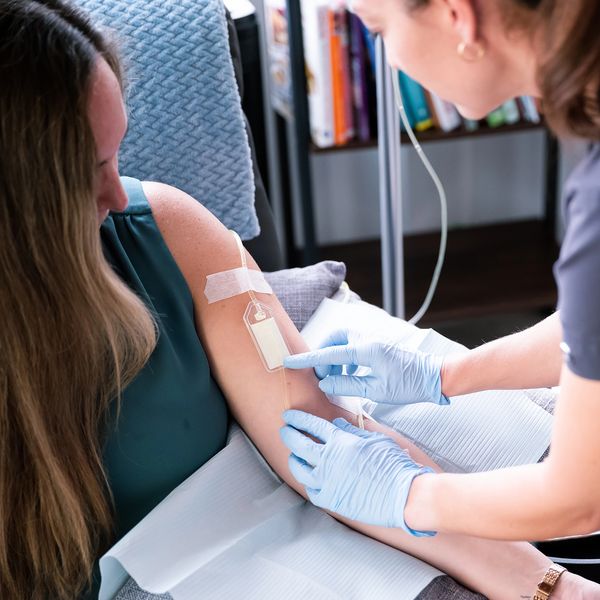 Nurse adjusting IV drip for patient in medical setting.