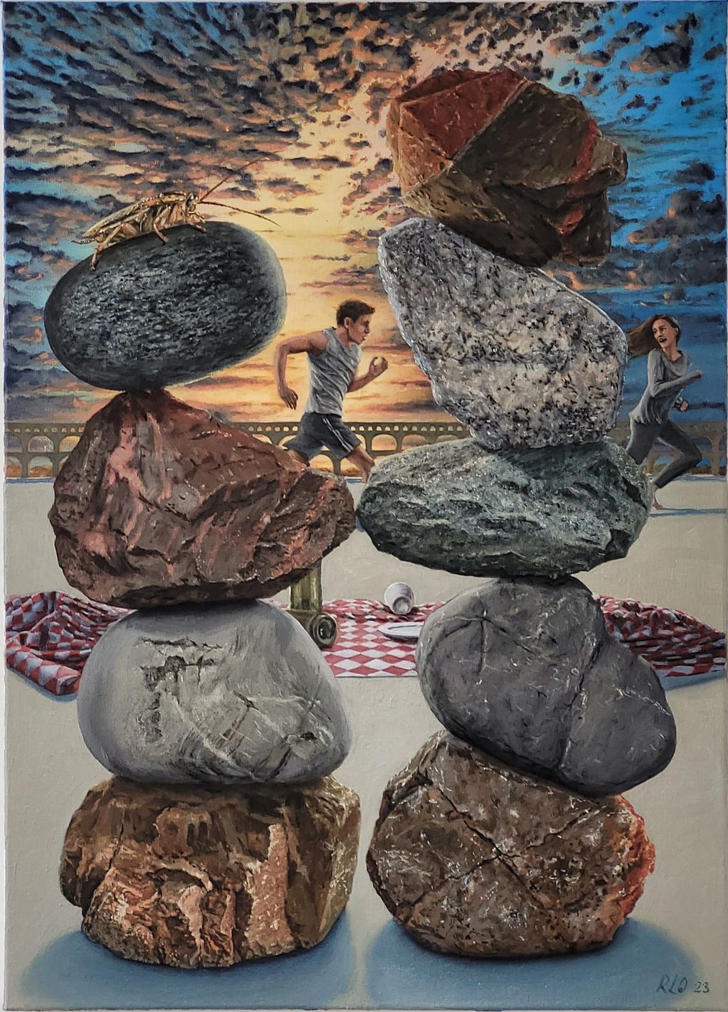 A stack of rock in front of a picnic blanket, a man running after woman in the back