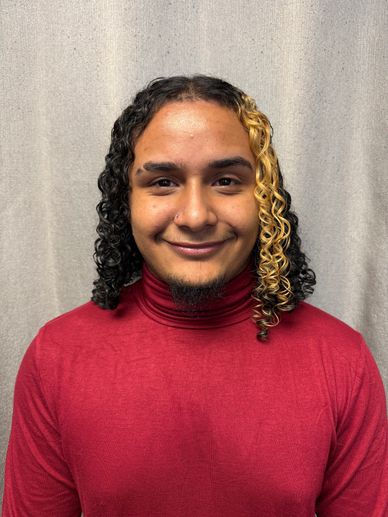 Person with curly, half-blond hair wearing a red turtleneck.