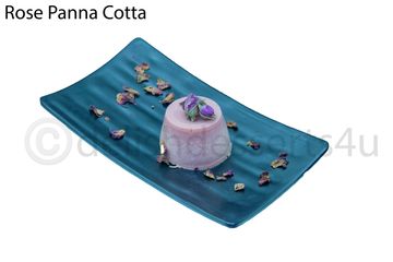 Elegant rose panna cotta dessert garnished with rose petals on a blue plate.