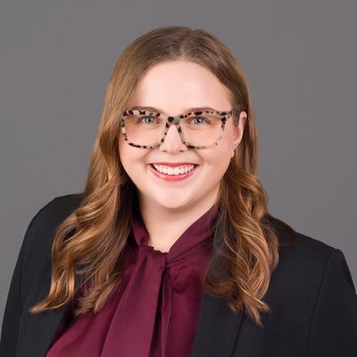 Professional woman with glasses and wavy hair smiles at the camera.