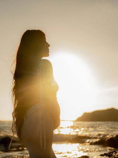 Silhouette of a pregnant woman standing by the ocean at sunset.