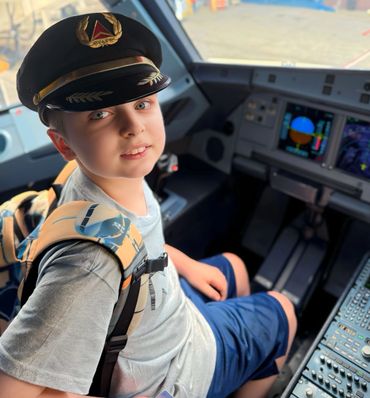 A young boy wearing a pilot's hat sitting in an airplane cockpit.