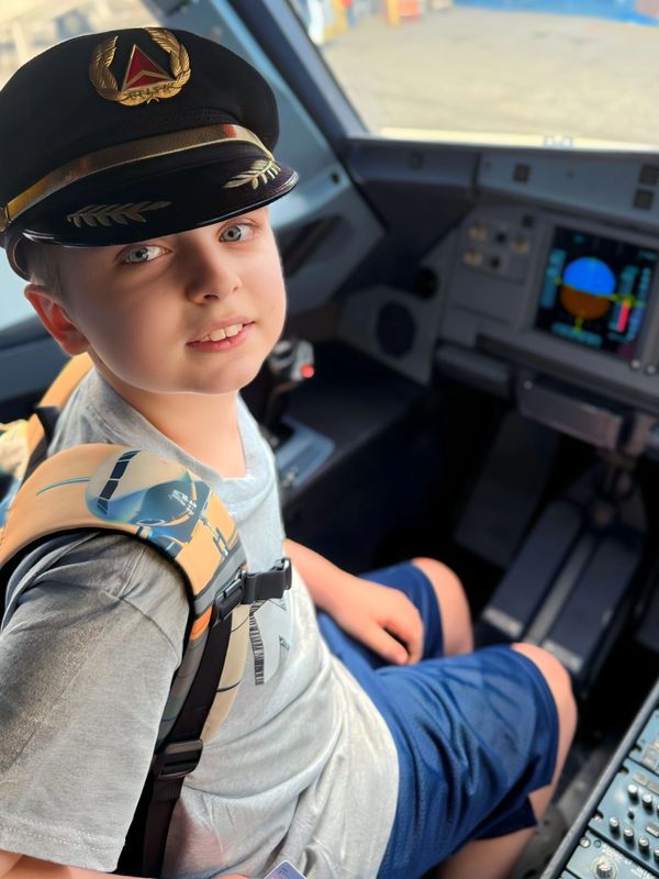 A young boy wearing a pilot's hat sits inside an airplane cockpit.