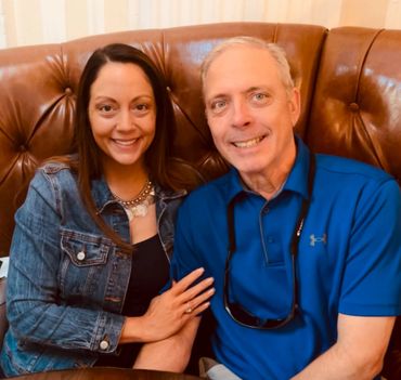 A smiling couple sitting on a brown leather couch.