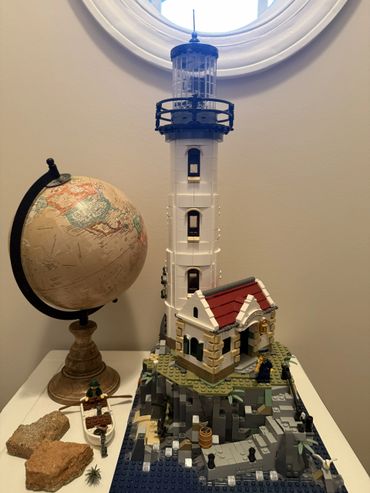 Lego lighthouse model with a globe and small boat on a table.