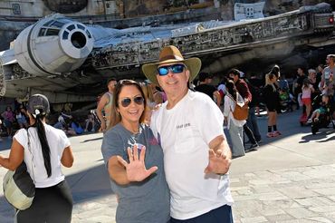 Couple posing happily in front of the Millennium Falcon at a theme park.