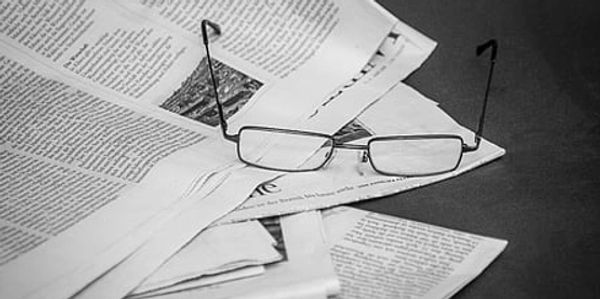 Reading glasses resting on scattered newspapers in black and white.