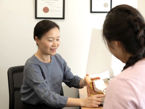A woman explains a foot model to another woman in a clinical setting.