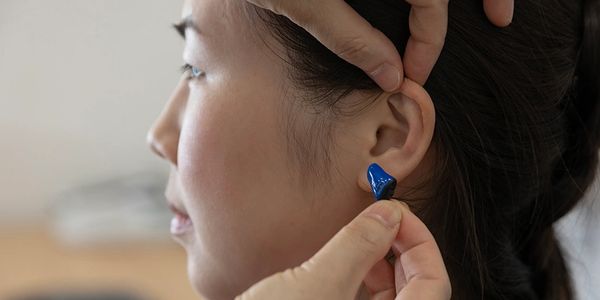 Person inserting a blue earbud into their ear.